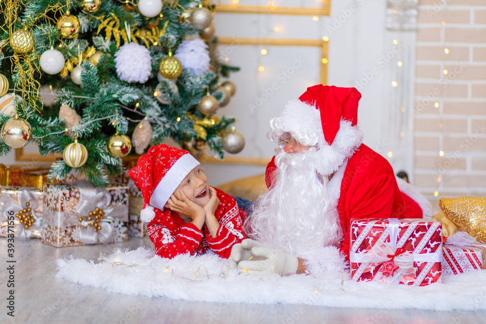 Obraz premium child and Santa Claus near the Christmas tree, boy looks at Santa Claus
