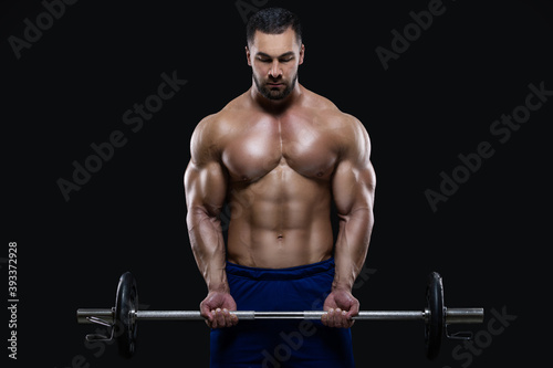 Handsome fitness man is standing with a heavy barbell ready to workout isolated on black background