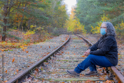 Side view of an adult woman sitting on the train track, mask and glasses, gray-black hair, old Iron Rhine railway (IJzeren Rijn), autumnal trees in Meinweg nature reserve, Middle Limburg, Netherlands photo