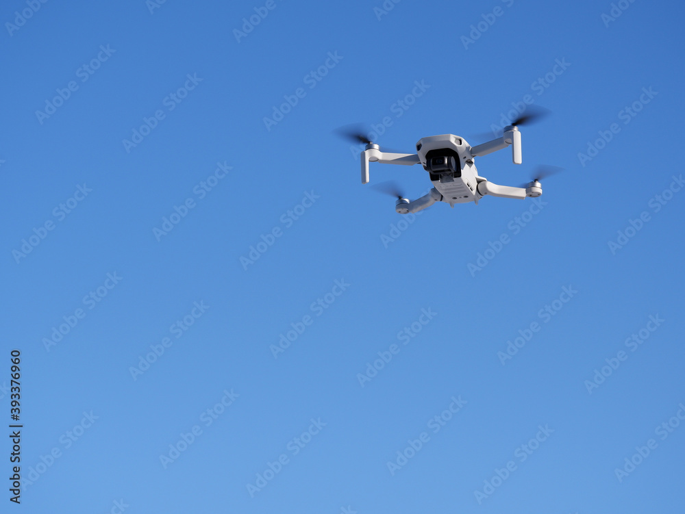 A white quadcopter shoots video in the blue sky. Part of the image is blurred. A white quadcopter shoots video in the blue sky. Part of the image is blurred.