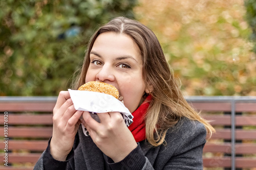 Young hungry woman eats Burger and takes lunch break outdoors in Park.Fast food. Takeaway food concept