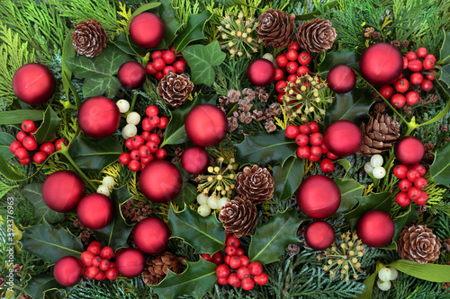 Festive Christmas background with red ball bauble decorations   winter flora of holly  ivy  mistletoe  cedar leaves   pine cones. Traditional composition for the solstice and New Year. Top view.