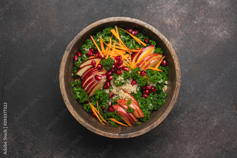 Kale salad with quinoa, apples, carrots and pomegranate seeds in wooden bowl. Nutritious vegan seasonal food. Brown background, top view, copy space Kale salad with quinoa, apples, carrots and pomegranate seeds in wooden bowl. Nutritious vegan seasonal food. Brown background, top view, copy space