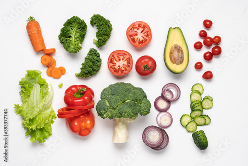 Creative layout made of variety of vegetables for making salads. Carrots, lettuce, kale, tomato, cucumber, broccoli, avocado, red bell pepper, onion. White background, top view, copy space