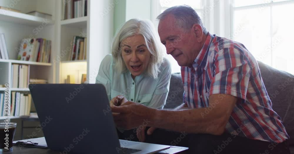 Senior couple with laptop using calculator and checking finances while sitting on the couch at home Senior couple with laptop using calculator and checking finances while sitting on the couch at home