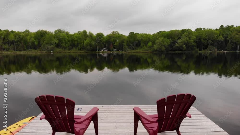 A shot flying over a dock with 2 chairs and heading towards the centre of a lake.