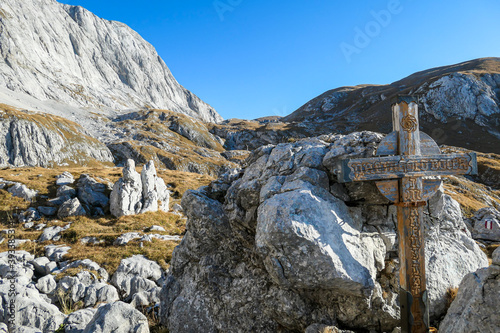 Small, wooden cross on top of a passage in the region of Hochschwab in Austrian Alps. There are massive stony wall in the back. The flora overgrowing the slopes is golden. Spirituality, memory place photo