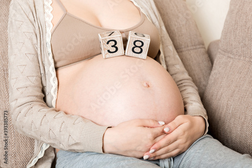 Pregnant woman in white underwear on bed in home holding calendar with weeks 38 of pregnant. Maternity concept. Expecting an upcoming baby photo