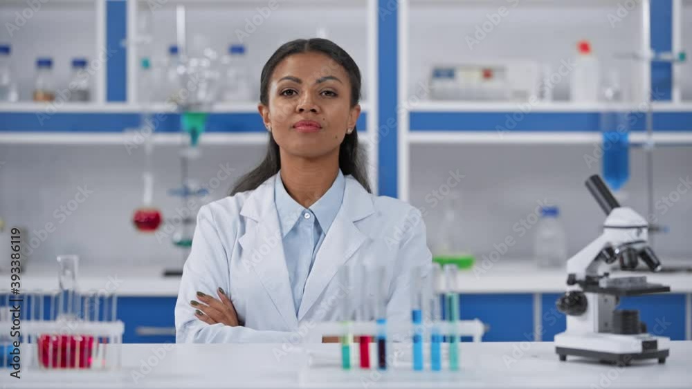 African american woman in white coat sitting with crossed arms in laboratory