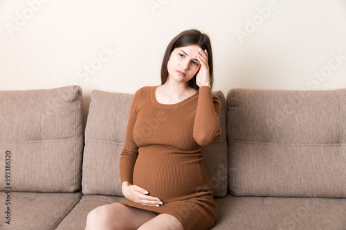 Young pregnant woman suffering from headache on sofa in home. Maternity healthcare concept © sosiukin