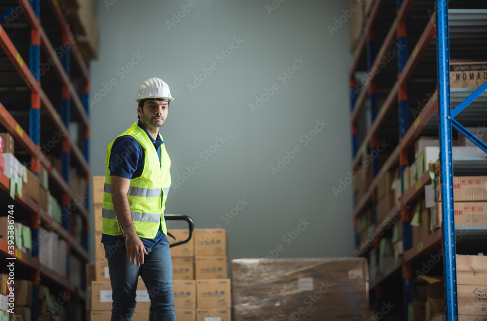 Young male worker in uniform is in the warehouse pushing pallet truck
