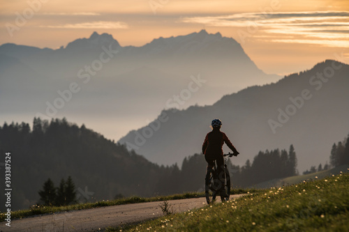 active woman riding her electric mountain bike at sunset in front of the awesome silhouette of Mount Saentis, Appenzell switzerland