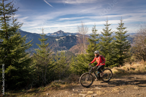 pretty senior woman riding her electric mountain bike in the mountains of East Allgaeu on warm autumn day with Mount Zugspitze in background