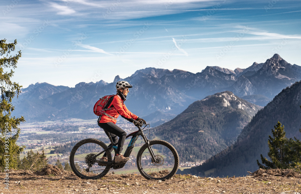 pretty senior woman riding her electric mountain bike in the mountains of East Allgaeu on warm autumn day with Mount Zugspitze in background