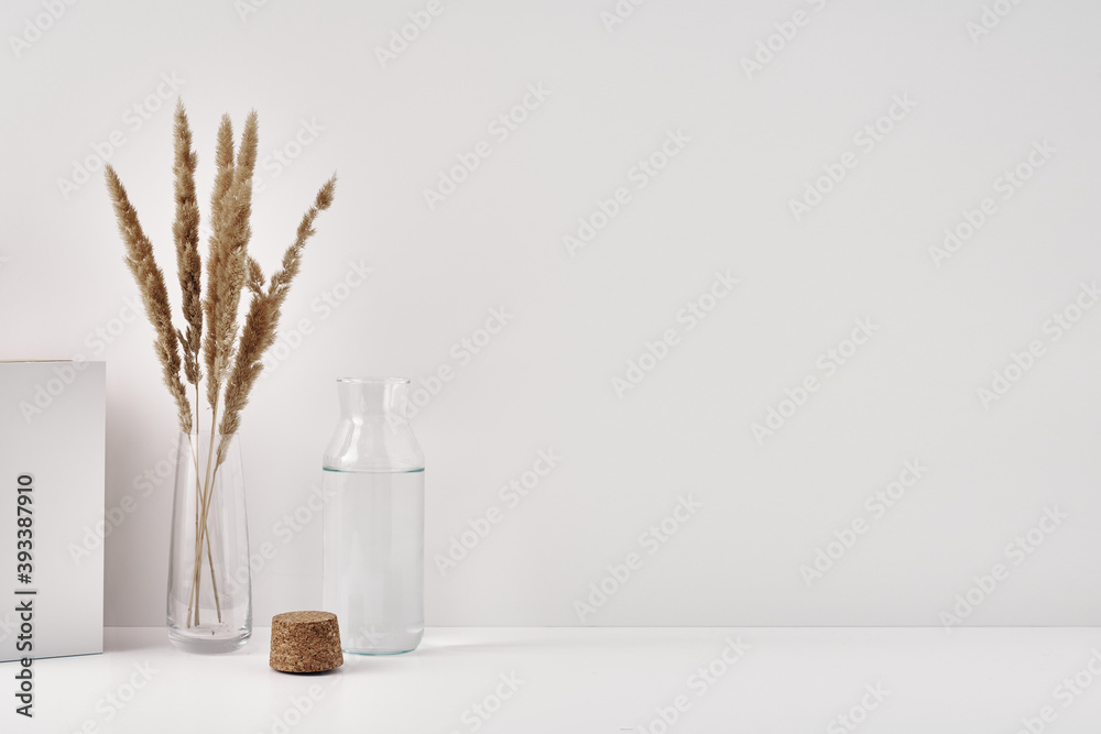 A transparent vase with spikelets and a bottle of water with a cork stopper on a white background. Minimalism, eco-materials in the interior decor. Copy space, mock up.