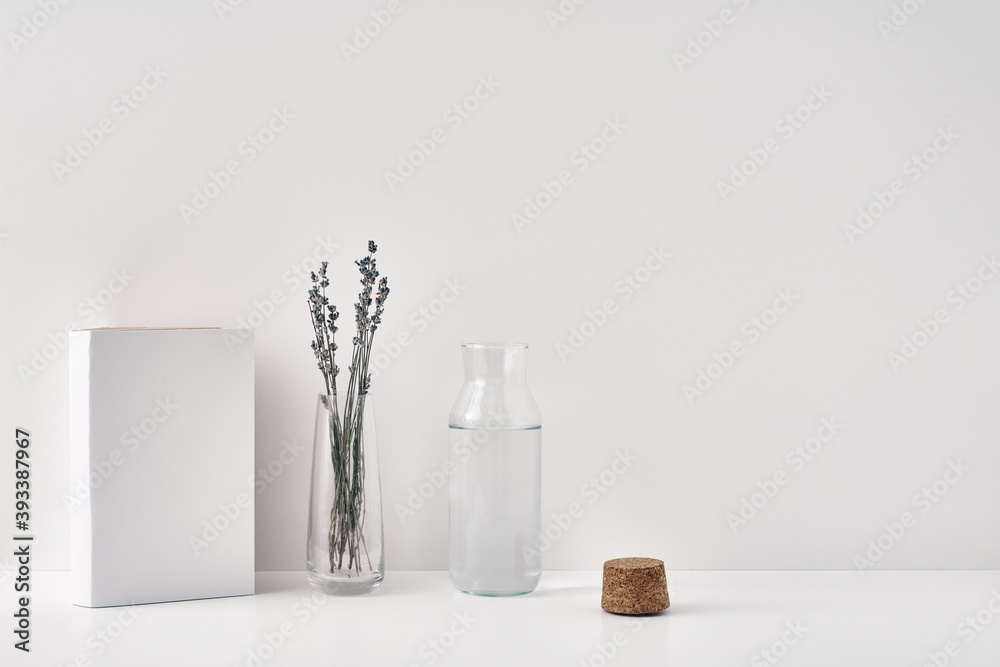 A transparent vase with lavender, a bottle of water with a cork stopper and a book on a white background. Minimalism, eco-materials in the interior decor. Copy space, mock up.