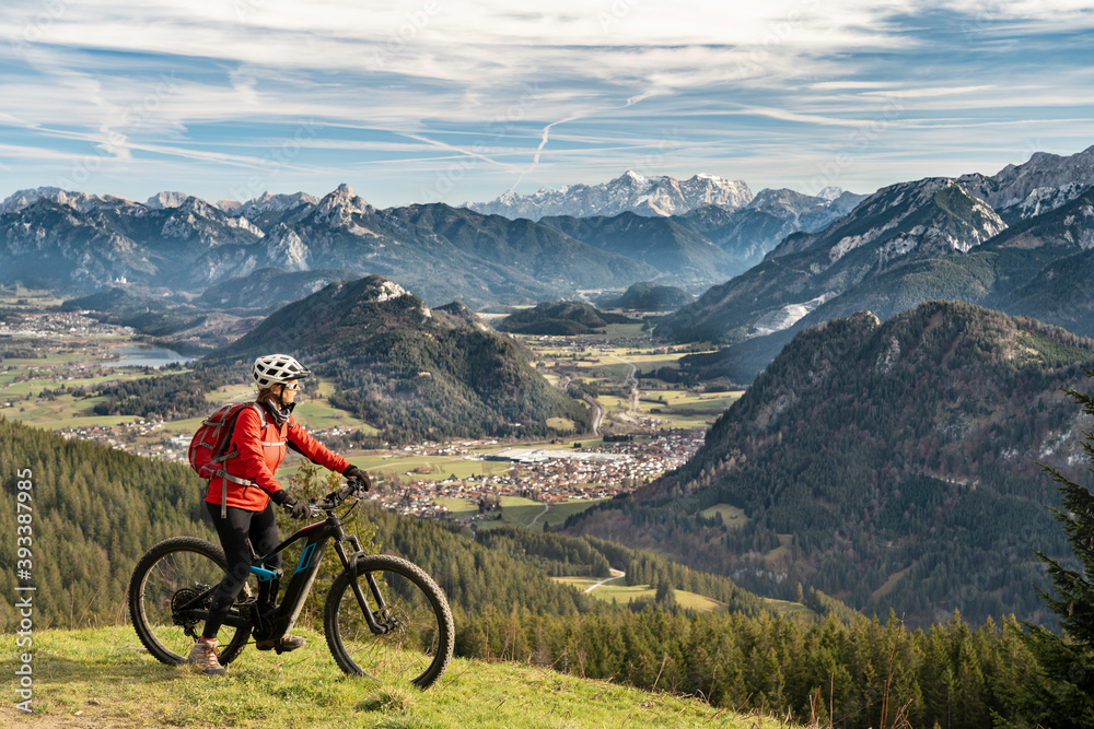 pretty senior woman riding her electric mountain bike in the mountains of East Allgaeu on warm autumn day with Mount Zugspitze in background