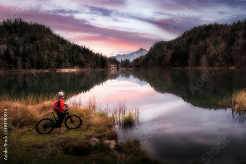 woman with mountain bike enjoying sunrise over lake Alatsee in the eastern Allgaeu near city of Fuessen