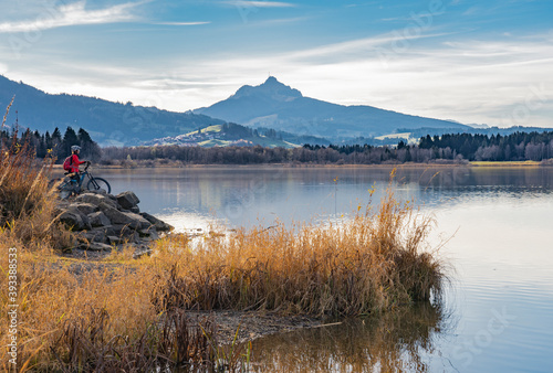 nice senior woman with electric mountain bike enjoying the view over autumnal lake Gruentensee in the Allgaeu alps near Nesselwang, Bavarian Alps, Germany photo