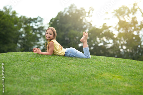 Canvas Print Cute little girl in casual clothes lying on the green lawn and smiling at camera