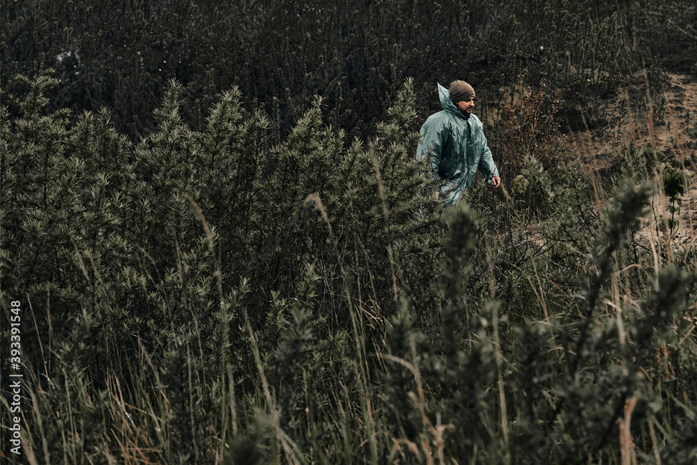 Obraz premium A man in a green raincoat walks along a country road, cloudy, autumn.