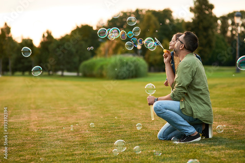 Fotografi Young father and his little girl having fun while blowing soap bubbles on a summ