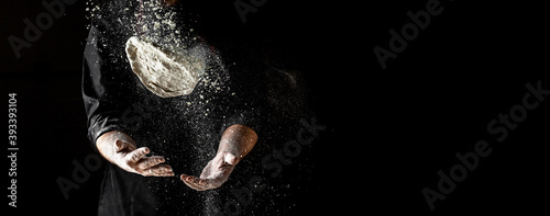 flying pizza dough with flour scattering in a freeze motion of a cloud of flour midair on black. Cook hands kneading dough. copy space photo