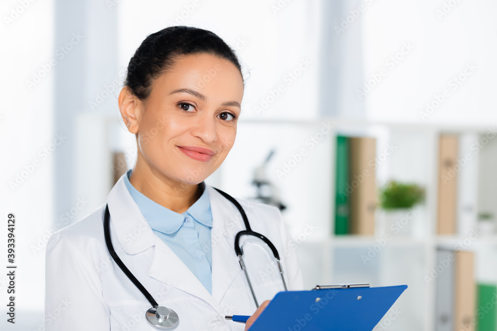 Portrait of smiling african american doctor with clipboard looking at camera on blurred background Portrait of smiling african american doctor with clipboard looking at camera on blurred background