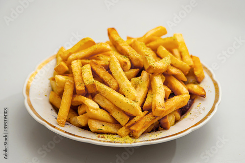 The fried fries are on a white plate and sprinkled with seasoning.