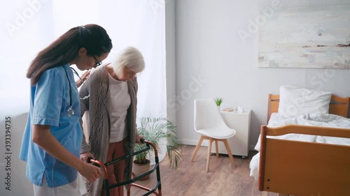 brunette geriatric sister helping woman stepping with walkers