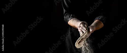 Obraz  z motywem Beautiful and strong men's hands knead the dough make bread, pasta or pizza. Powdery flour flying into air. chef hands with flour in a freeze motion of a cloud of flour midair