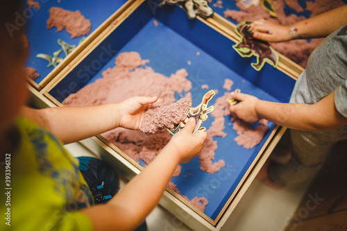 children moulds from plasticine on table, Child hands playing with colorful clay, day care close up, tactility activity with dinosaur figures