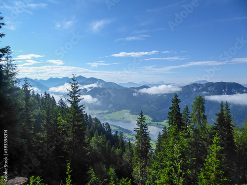 An idyllic view from the side of the mountain on a distant Weissensee lake in Austria. The lake is surrounded by high Alps. Few clouds above the peaks. High mountains around. Calmness