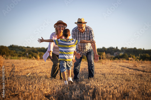 Grandparents having fun with the grandson. They're playing on the meadow and joying in sunset.	 photo