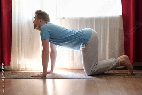 man practices yoga asana marjariasana or cow pose at home. photo