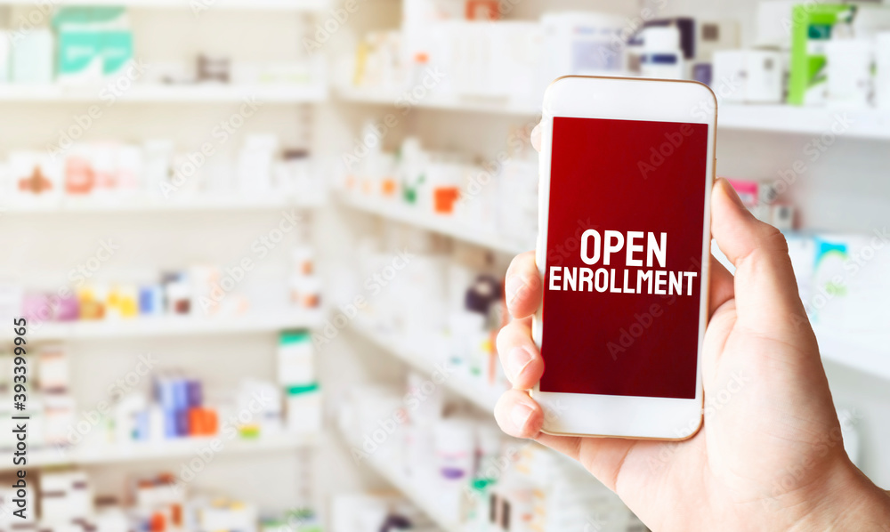 hand holding smart phone in pharmacy drugstore. Text OPEN ENROLLMENT