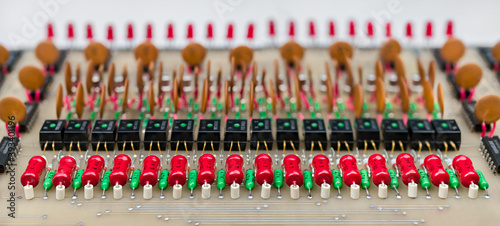 Power resistors, optocouplers or ceramic capacitors in rows. Vintage circuit board. Old electronic device for data links galvanic isolation. Colored electrical components in panoramic detail. E-waste.