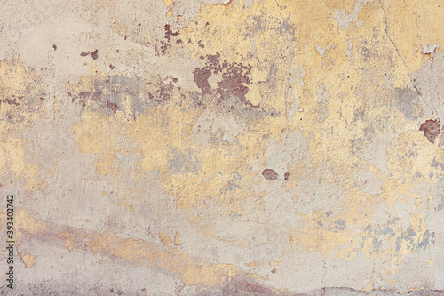 Old cracked weathered painted wall background texture. Yellow dirty peeled plaster wall with falling off flakes of paint