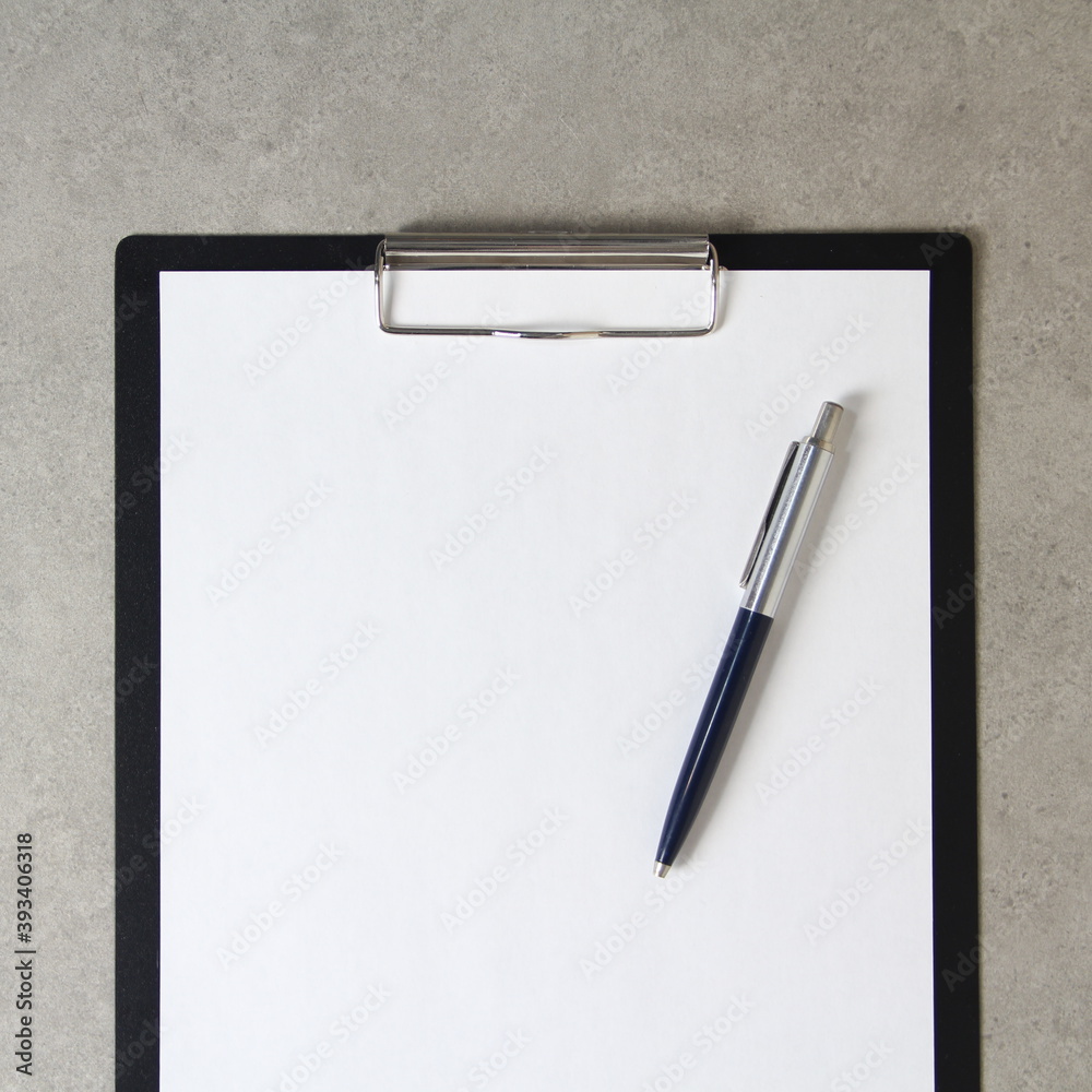 Template of white paper with a ballpoint pen on light grey concrete background in a black tablet with a clip. Concept of new idea, business plan and strategy, empty space for text