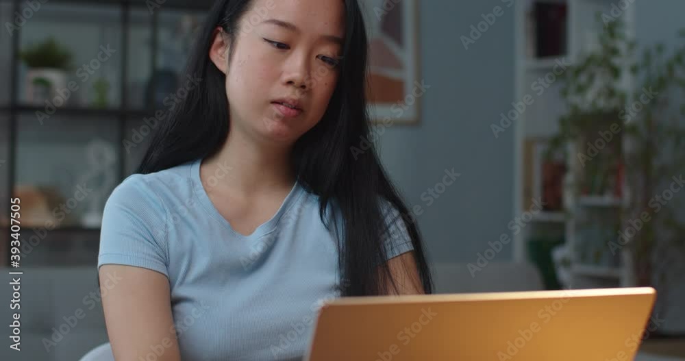 Close up portrait of serious concentrated Asian female student texting on laptop indoors in cabinet in good mood. Young woman typing on computer in room. Distance learning. Work concept Close up portrait of serious concentrated Asian female student texting on laptop indoors in cabinet in good mood. Young woman typing on computer in room. Distance learning. Work concept
