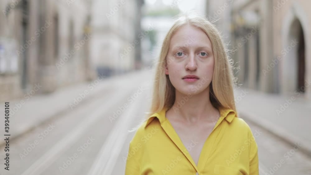 Crop view of serious blonde hair woman looking to camera. Portrait of pretty female person in bright yellow outfit posing while standing outdoors. Blurred background. Crop view of serious blonde hair woman looking to camera. Portrait of pretty female person in bright yellow outfit posing while standing outdoors. Blurred background.