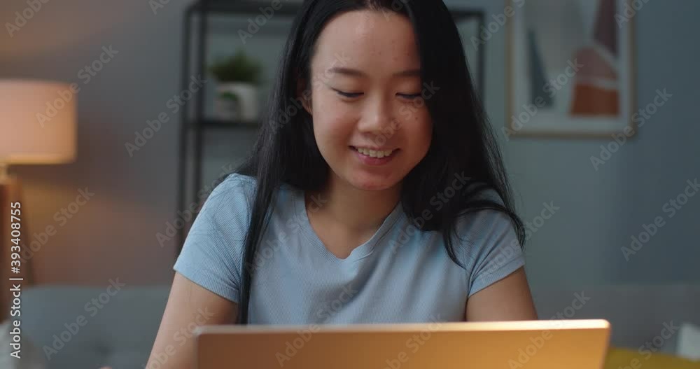 Close up of happy smiling female making purchase online and paying with credit card while typing on laptop indoors. Asian joyful woman buying stuff on internet on computer. Shopping online concept
