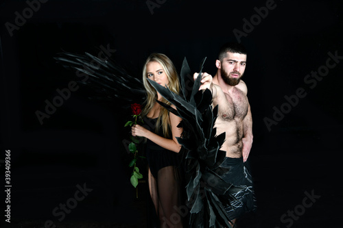 beautiful girl in angel costume with black wings and handsome muscular man struggling with difficulties on a black background
