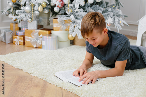 teenager reads a book while lying on the floor near the new year tree. christmas and new year concept. Light Christmas interior.