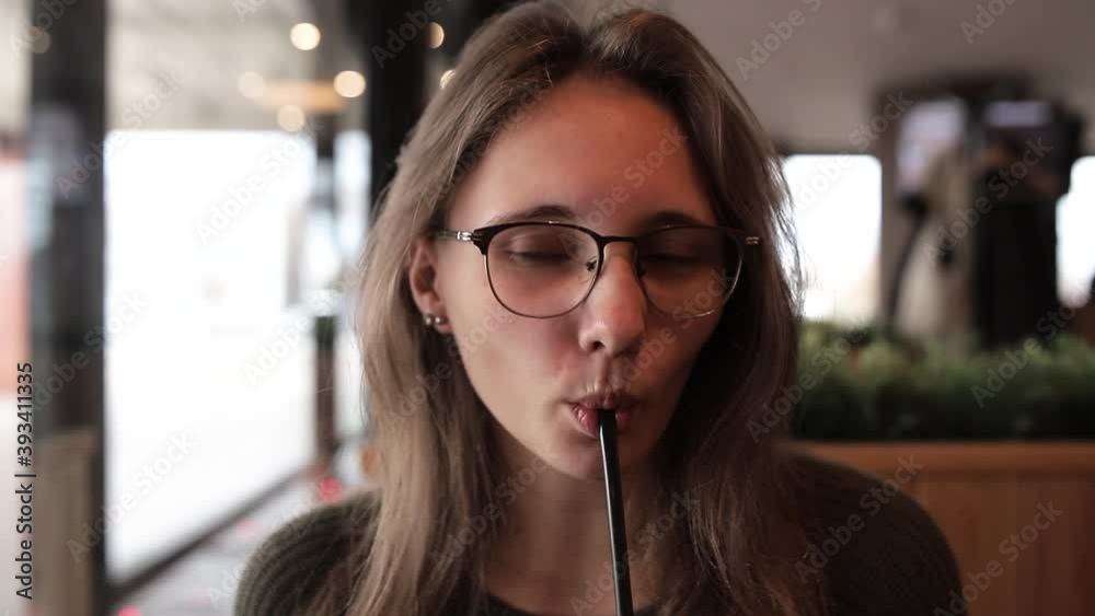 A young girl with glasses is sitting in a coffee shop by the window A young girl with glasses is sitting in a coffee shop by the window