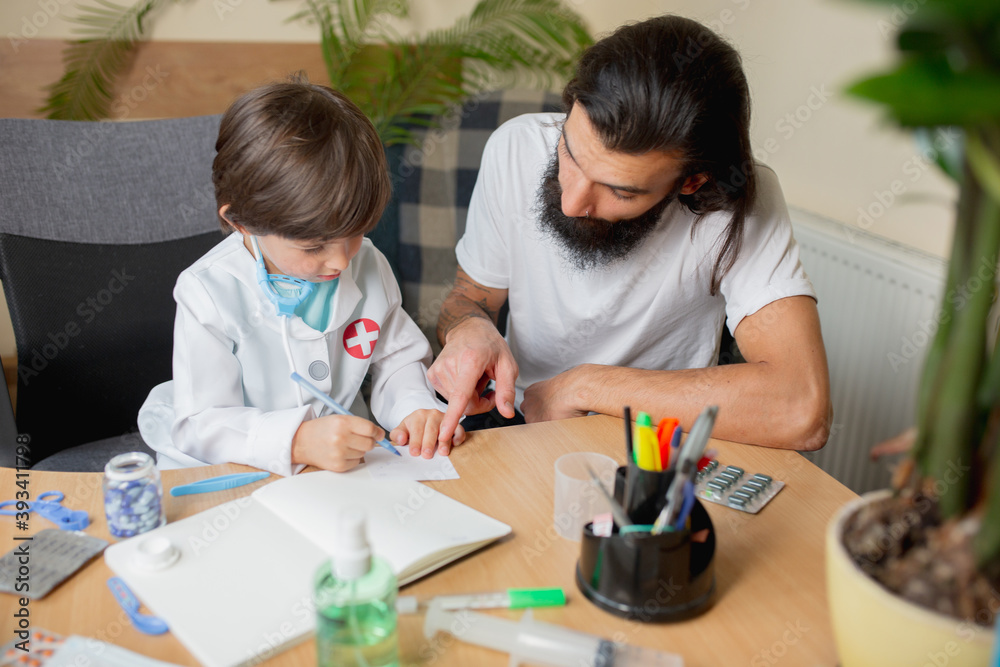 Little boy playing pretends like doctor examining a man in comfortabe medical office. Healthcare, childhood, medicine, protection and happiness concept. Having fun, laughting while giving pills recipe Little boy playing pretends like doctor examining a man in comfortabe medical office. Healthcare, childhood, medicine, protection and happiness concept. Having fun, laughting while giving pills recipe