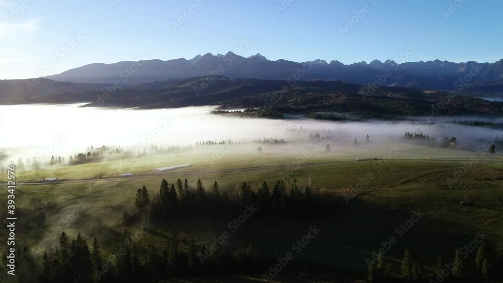 Mountains landscape with morning fog, aerial view. Tatra high mountains in the sunny morning after sunrise. Alpine scenery after dawn. Bird eye view of misty forest and hight mountains in background. Mountains landscape with morning fog, aerial view. Tatra high mountains in the sunny morning after sunrise. Alpine scenery after dawn. Bird eye view of misty forest and hight mountains in background.