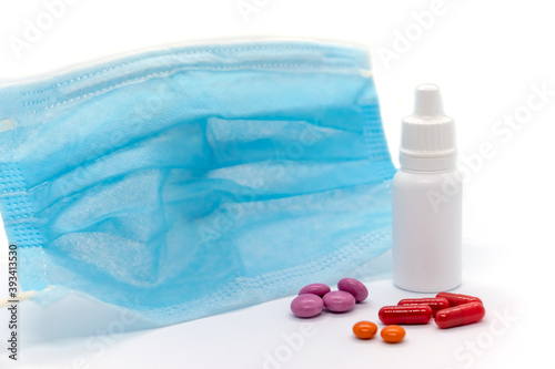 Medical mask, multicolored pills, nasal drops for the common cold on white background