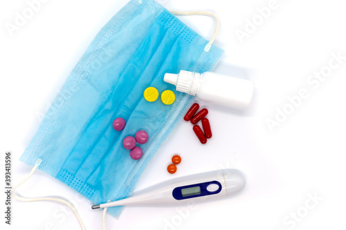 Medical electronic thermometer, medicine, medical mask, drops and pills on white background. Top view.