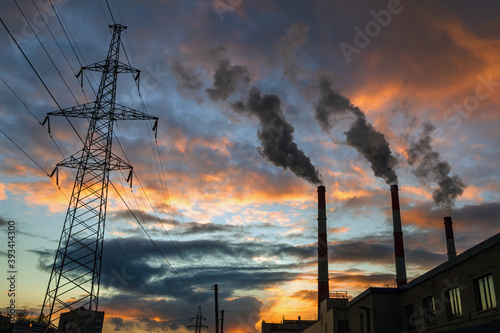 Silhouette of steel lattice tower, chimneys smoke on sunset sky background. Transmission tower and industry pipes